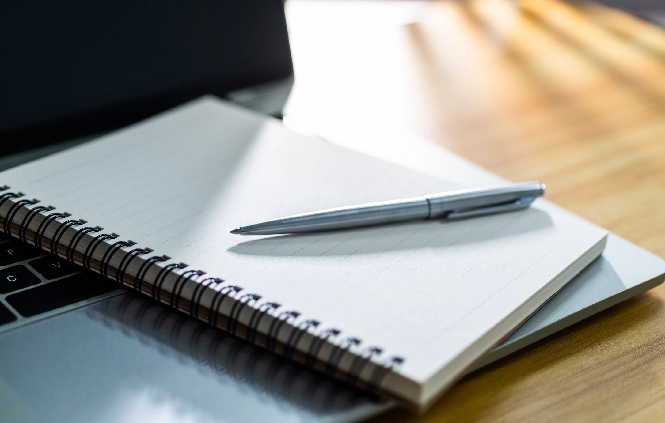 Open notebook with pen beside a laptop on a desk
